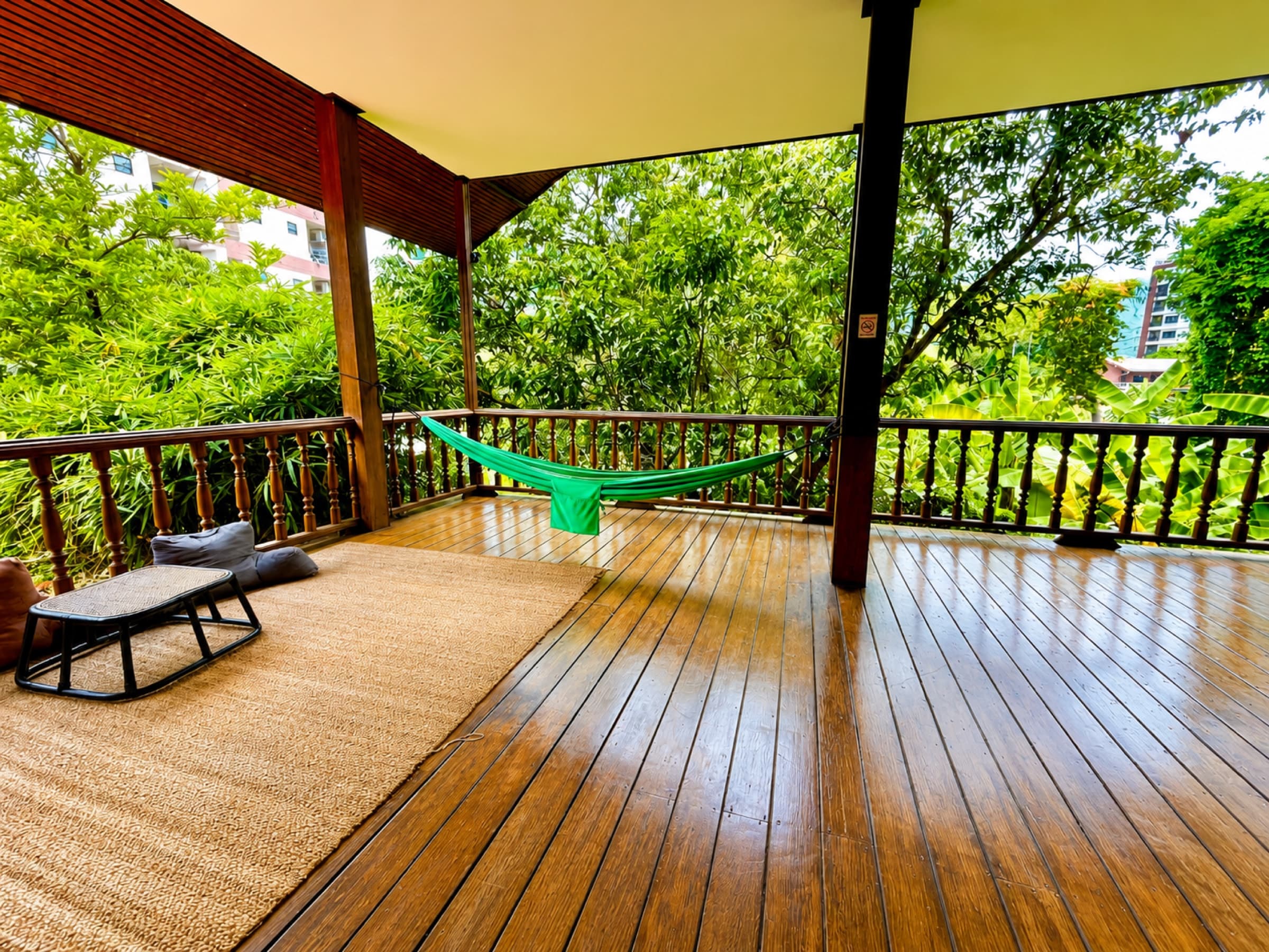 Wooden upstairs terrace with green hammock, woven rug and view onto the trees